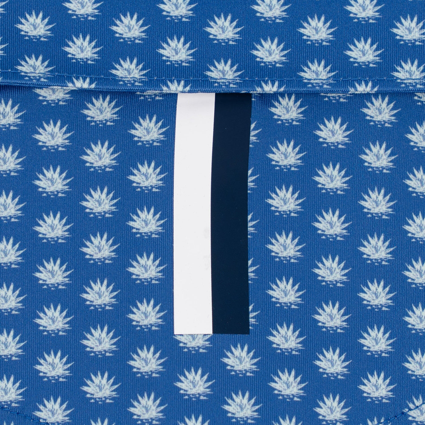 Close-up of RHOBACK’s The Agave 2.0 Performance Polo in Short Stop Blue/Seafoam, featuring a repeating white leaf pattern on moisture-wicking fabric and a vertical black-and-white stripe partially covered by a horizontal flap.