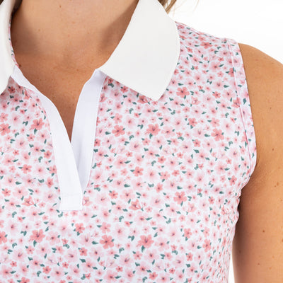 A close-up of the RHOBACK Brooke Sleeveless Performance Polo | The Azalea 2.0 in White/Pearl Pink, featuring a white collar, pink floral pattern, V-neck opening, and moisture-wicking fabric for all-day comfort on light skin.