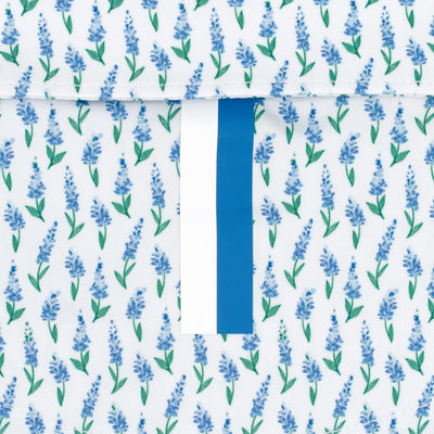 A close-up of RHOBACK's The Blue Bonnet 2.0 Performance Polo in White/Lake Blue, featuring moisture-wicking fabric with small blue flowers, green stems, and a central white strip with a vertical blue stripe for added style.