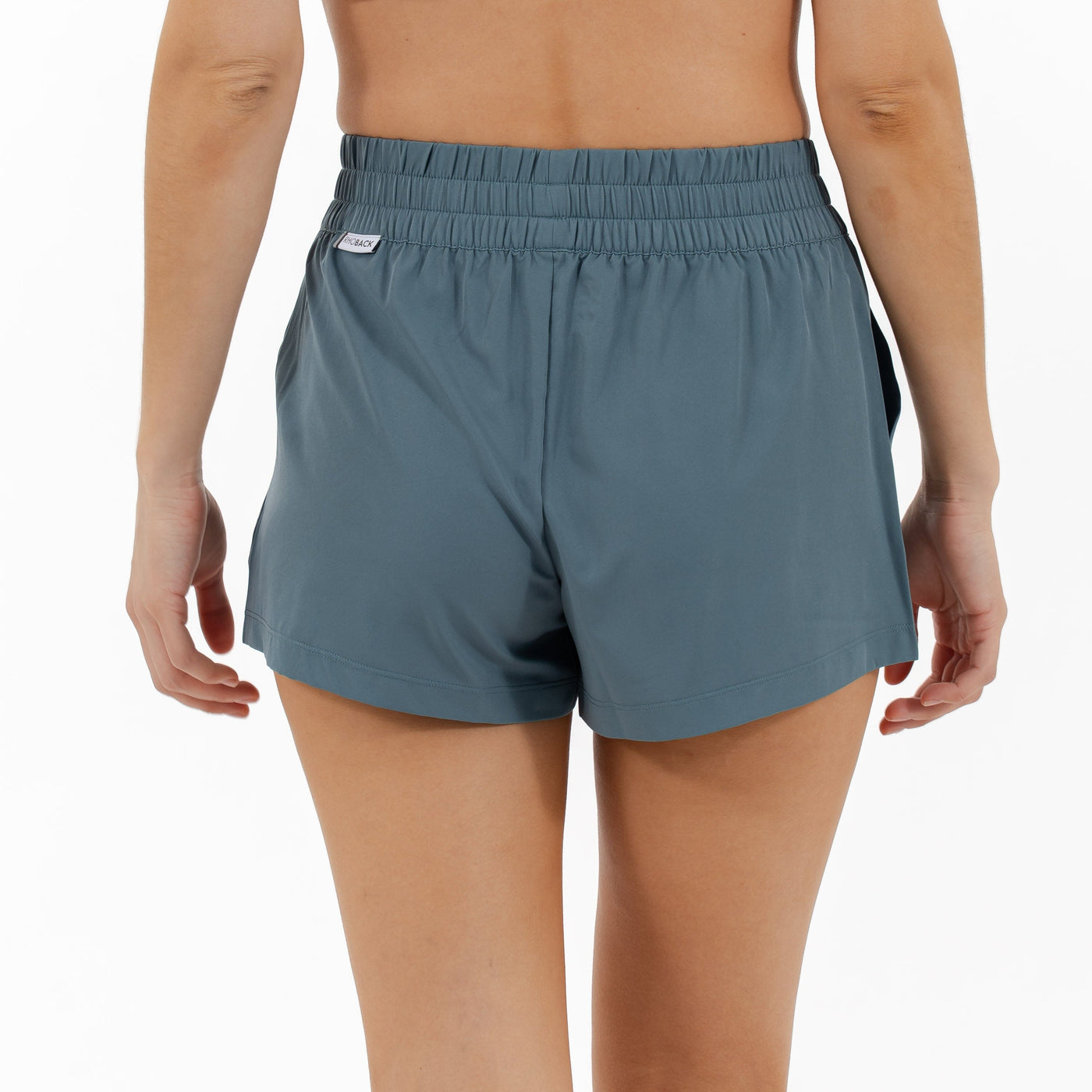 A person faces away from the camera, wearing RHOBACK's Era High-Rise Short | Solid in Jungle Green, featuring four-way stretch fabric and an elastic waistband, set against a plain white background.