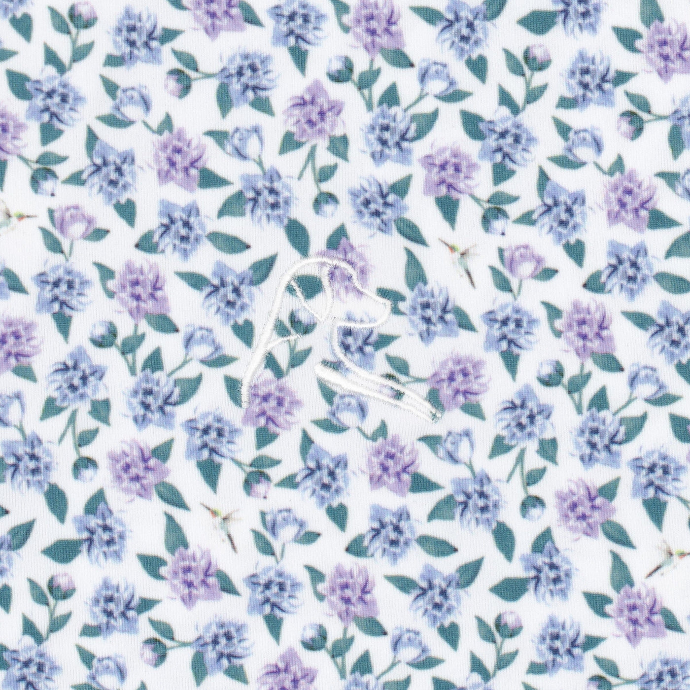 The Flutter Floral Performance Polo by RHOBACK features a white embroidered bird on moisture-wicking fabric with small purple flowers and green leaves over a pale background.
