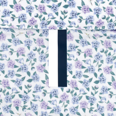 A close-up of RHOBACK’s The Flutter Floral Performance Polo in White/Air Blue shows moisture-wicking fabric with tiny purple and blue flowers, green leaves, and a vertical black-and-white stripe for stylish sun protection.