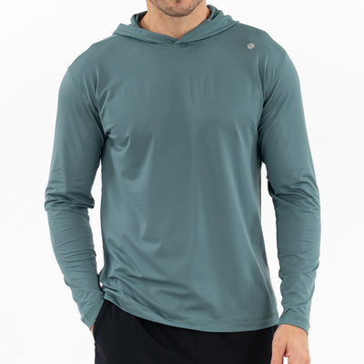 A man wears a RHOBACK Blitz Tech Hoodie in Heather - Jungle Green/Dusty Pine, made with SilverKnit fabric and ionic+ silver technology, plus black shorts. He stands against a white background with his face partially out of view.