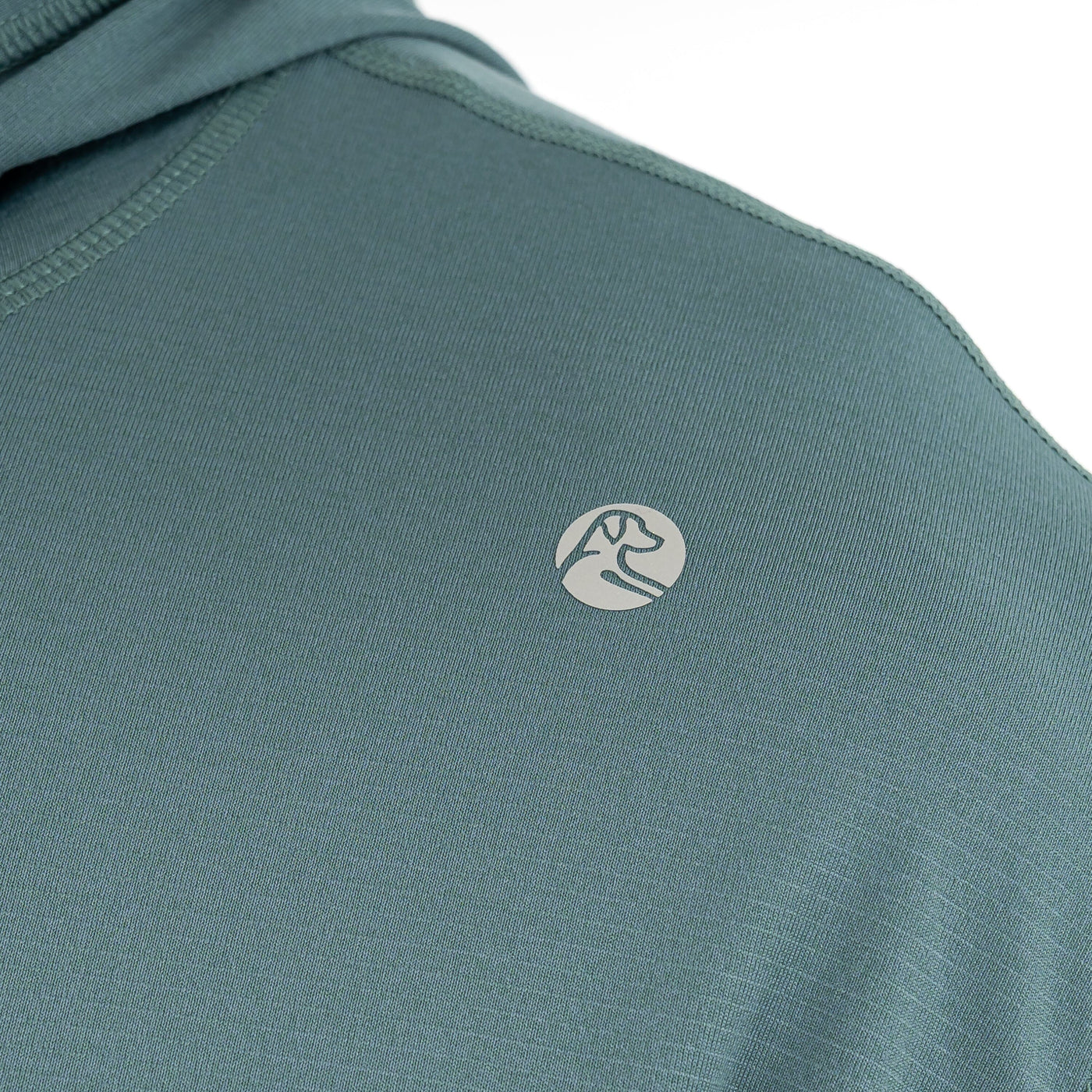 Close-up of the RHOBACK Blitz Tech Hoodie | Heather in Jungle Green/Dusty Pine, crafted from SilverKnit fabric and featuring a small, circular mountain and river logo near the shoulder.