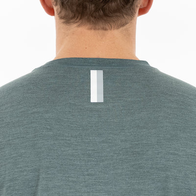 The back view shows a person in the RHOBACK Tailwind Performance Tee | Heather - Jungle Green/Dusty Pine, featuring moisture-wicking fabric and a vertical reflective strip near the neckline. The person's head and neck are partly visible.