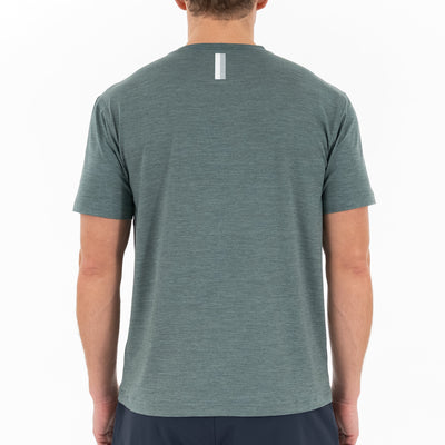 A person is shown from the back wearing the RHOBACK Tailwind Performance Tee in Heather - Jungle Green/Dusty Pine, featuring short sleeves, moisture-wicking SkyKnit™ fabric, and a small vertical reflective strip near the neckline on a white background.