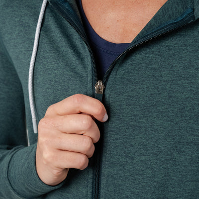 A person zips up the RHOBACK Tempo Performance Full-Zip Hoodie in Heather - Ponderosa Green/Willow Green, featuring VSoft fabric. The focus is on their hand and zipper, emphasizing the hoodie’s moisture-wicking comfort.