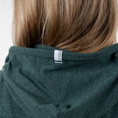 Close-up of the back of a person’s head with long, light brown hair, wearing the RHOBACK Tempo Performance Full-Zip Hoodie in Heather - Ponderosa Green/Willow Green, made from moisture-wicking VSoft fabric with a small white tag on the hood.