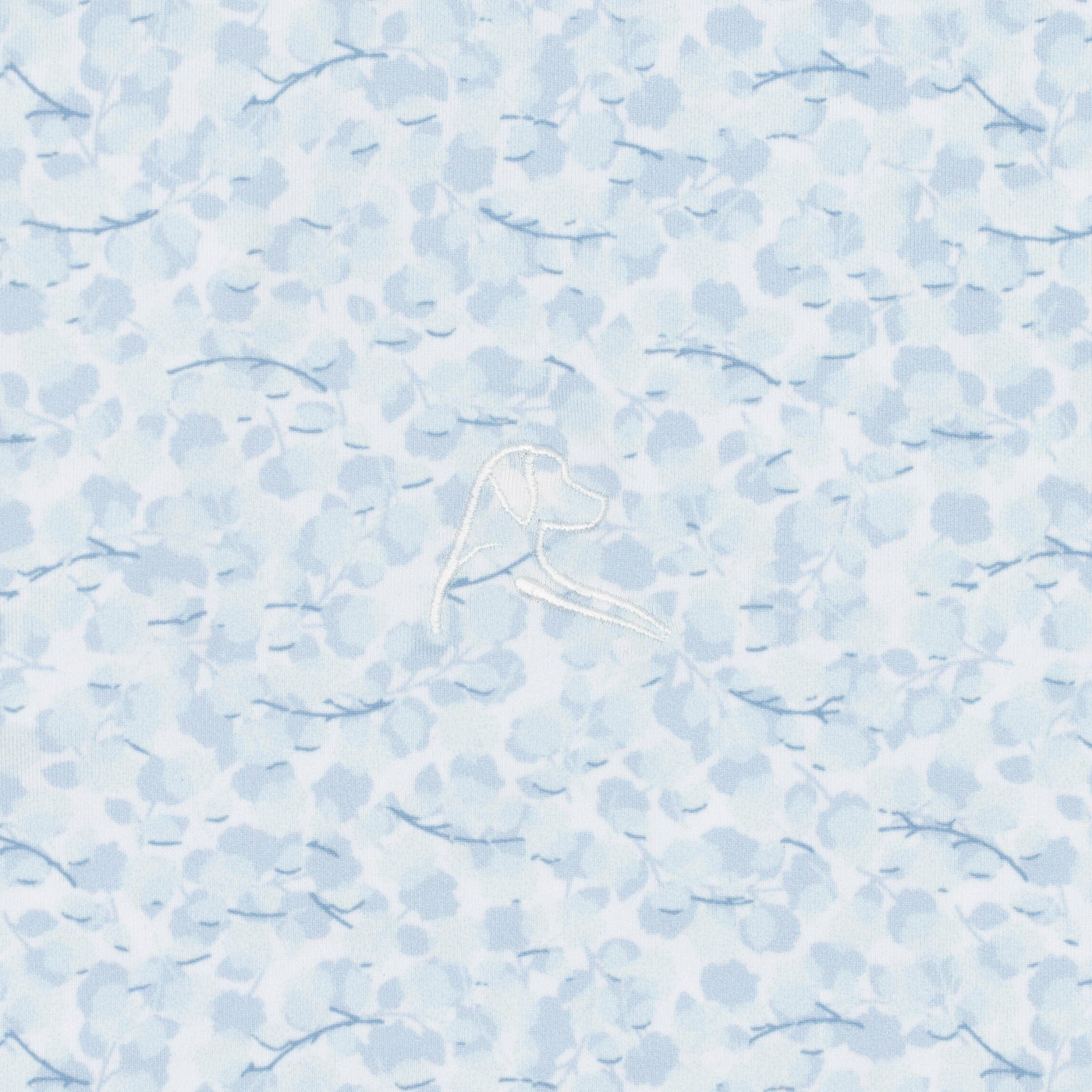 The RHOBACK Iridescence Performance Polo in White/Pure Blue features light blue patterned fabric with abstract shapes and small branches, plus a subtle white embroidered dog's head and breathable, moisture-wicking comfort.
