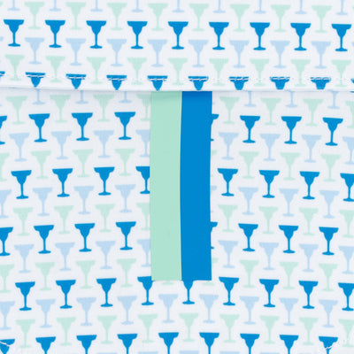 The Marg | Performance Polo by RHOBACK in White/Birdie Blue features repeating blue and teal cocktail glass silhouettes, a vertical mint-green and blue center stripe intersecting a top flap, and moisture-wicking fabric for comfort.