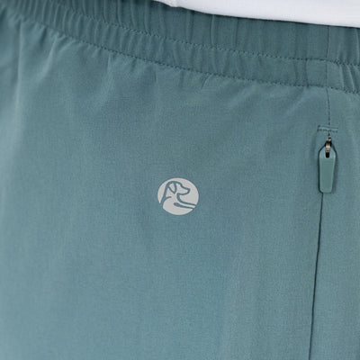 Close-up of RHOBACK All-Active Short in Jungle Green, crafted from quick-drying, lightweight fabric with an elastic waistband, zippered side pocket, and a small circular logo featuring a dog’s head outline.