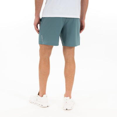 A person stands on a white background, seen from the back, wearing white sneakers, a white T-shirt, and RHOBACK All-Active Short | Solid in Jungle Green. The shorts are made with quick-drying, lightweight fabric.