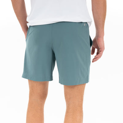 A person is shown from the back, hands in pockets, wearing a white t-shirt and RHOBACK All-Active Short | Solid - Jungle Green against a plain white background. The shorts feature lightweight, quick-drying fabric for active comfort.